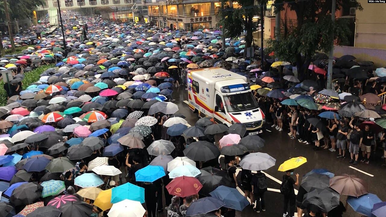 Une foule de manifestants sous des parapluies s'écarte pour laisser passer une ambulance dans une rue de Hong Kong